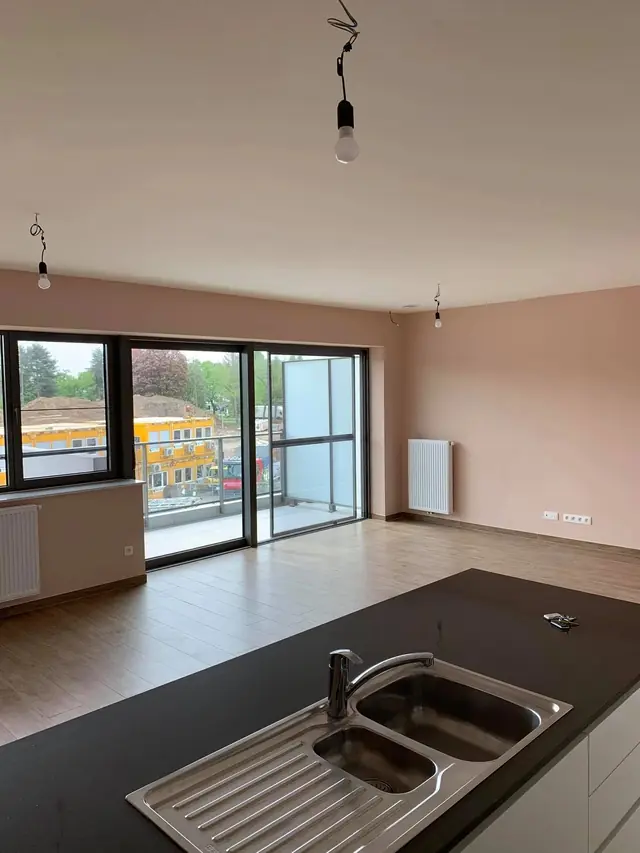 Schilderwerken Antwerpen: leefruimte met zachtroze muren en witte keuken na binnenschilderwerken