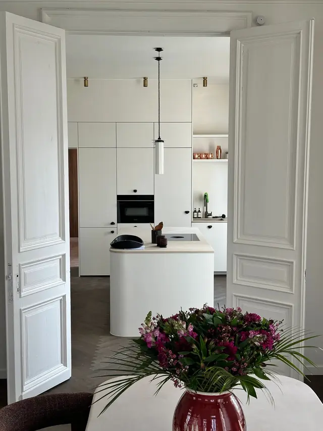 Schilderwerken Antwerpen: witte keuken met kookeiland achter openstaande witte paneeldeuren, geschilderd door Lecom Painting