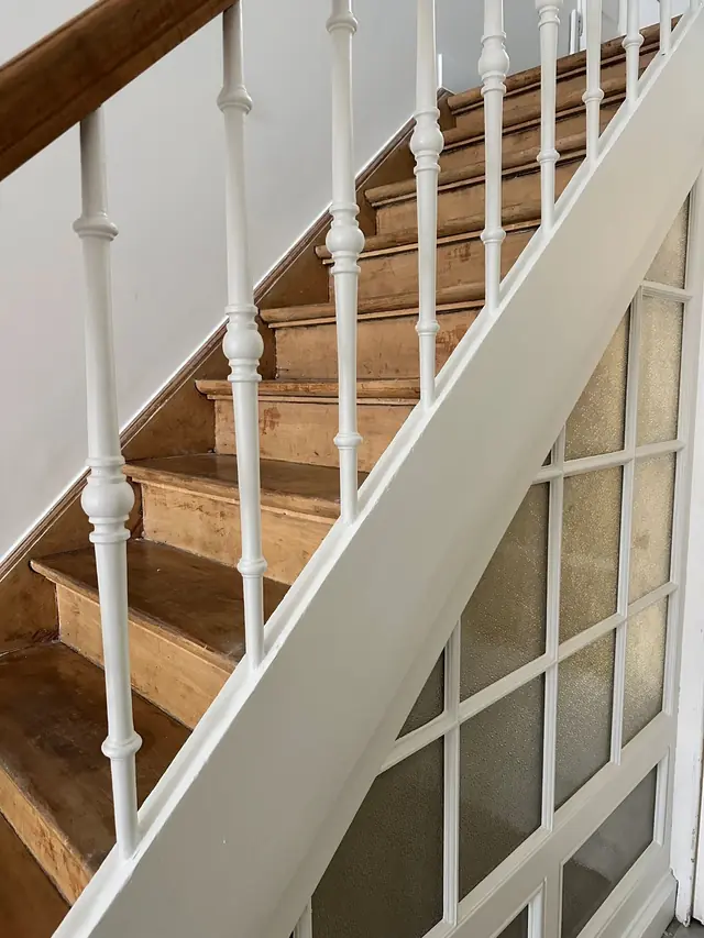 Trap met wit geschilderde balusters en houten leuning